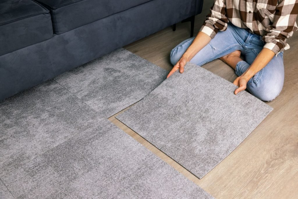 A woman is seated on a gray rug, highlighting carpet tile flooring services available in San Jose, CA.