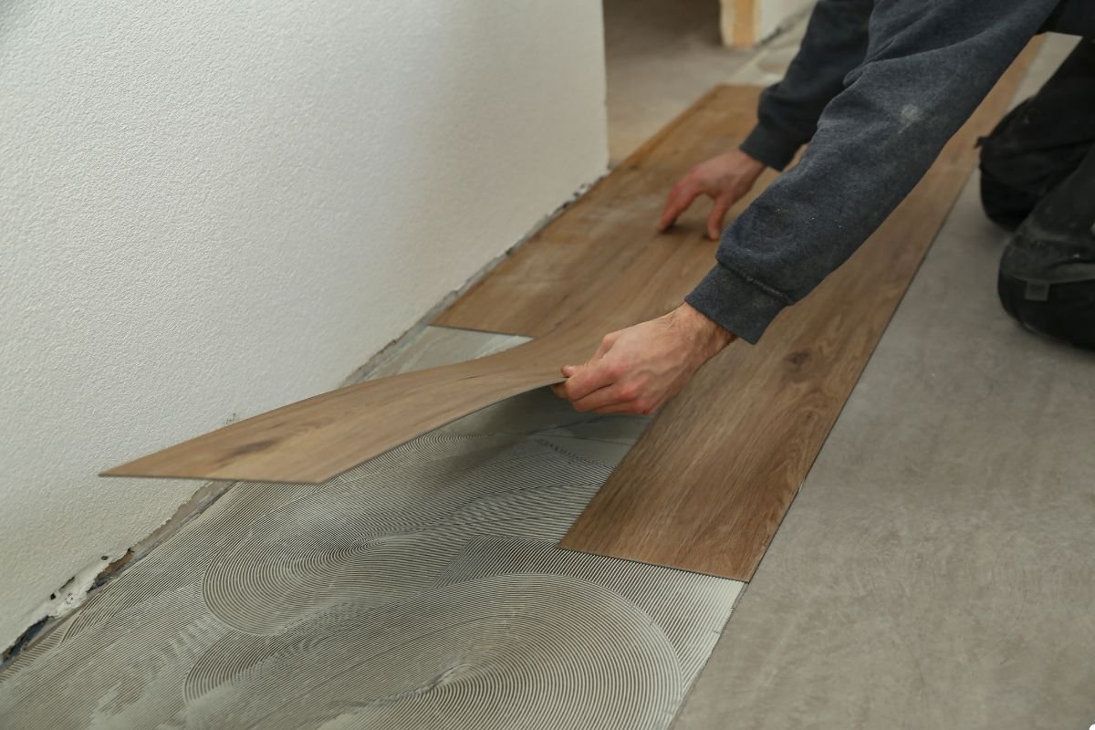 A man is installing a wooden floor, carefully laying down each plank with precision and focus.