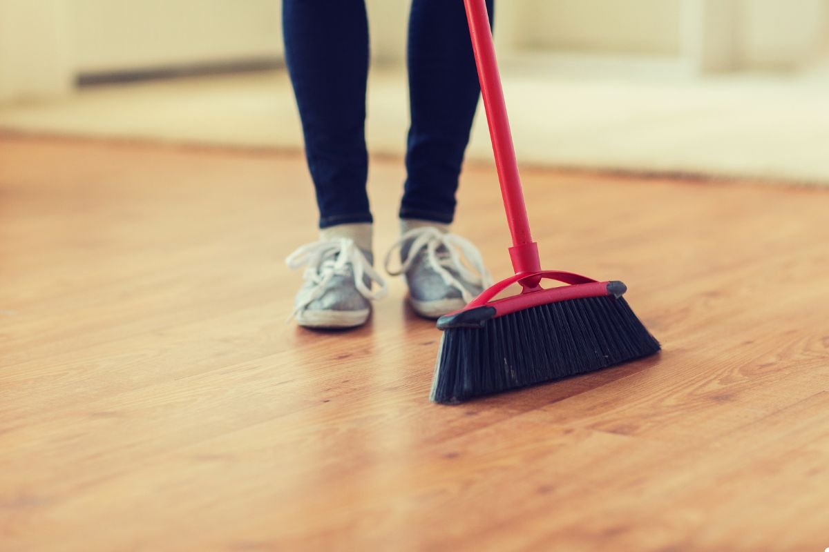 A woman uses a broom to sweep the floor, showcasing her commitment to keeping the area tidy.